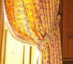 Yellow patterned curtain tied back with a decorative gold clasp.