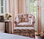 Armchair with floral pattern next to a side table with flowers, window, and a floor lamp.