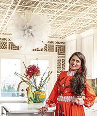Woman in orange dress in kitchen with ornate ceiling and floral arrangement.