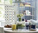 A dining room with a table set for breakfast. Blue and white decor with flowers and books.