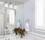 Bathroom with a large mirror, white and blue patterned tile, and a vase of flowers.