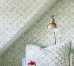 Bedroom corner with floral wallpaper, a beige lamp, and a quilted pillow.