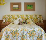 Bedroom with floral bedspread, headboard, and two framed landscape paintings above the bed.