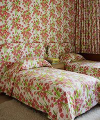Bedroom with floral wallpaper, matching bedding, and curtains; two twin beds are visible.