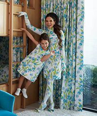 Woman and child matching floral outfits, posing by bunk bed and curtains.