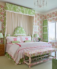 Bedroom with floral wallpaper and bedding in pink and green. Four-poster bed with bench.
