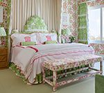 Bedroom with floral wallpaper, bed, bench, and curtains in shades of pink, green, and white.