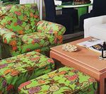 Green floral print armchair and footstools next to a wood coffee table, set in a room.