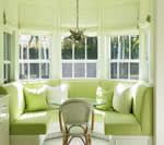 Bright green cushioned window seat with white pillows and a small chair. Light green curtains.