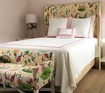 Bedroom with a floral upholstered headboard and bench, white bedding with pink trim, and a bedside lamp.