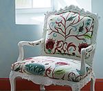 White ornate armchair with floral pattern against a light blue wall.