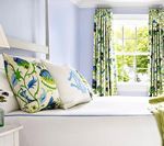 Bedroom with white bed and pillows, blue walls, patterned green curtains, and a window with a view.