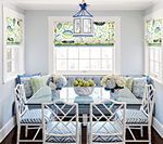 Dining nook with a glass-topped table, built-in bench seating, floral roman shades, and a blue lantern.
