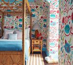 Bedroom with canopy bed, colorful floral wallpaper, blue and white bedding, and nightstand.