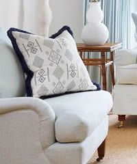Close-up of a white armchair with a patterned throw pillow with blue trim.