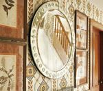 Round mirror reflecting a staircase, hung on patterned wallpaper with framed artwork.