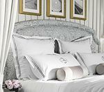 Bed with white linens, decorative headboard, and framed art.