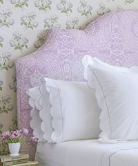 Lavender paisley headboard with white scalloped pillows and floral wallpaper.