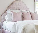 Bedroom with a detailed pink headboard, white bedding, and pink patterned pillows.