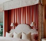 Bed with pink curtains and patterned headboard, topped with a fabric canopy.