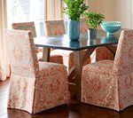 Dining room table with chairs covered in patterned fabric, vase of greenery, and decorative bowl.