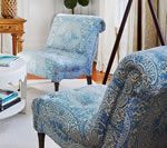 Two blue paisley armchairs in a living room, next to a side table and lamp.