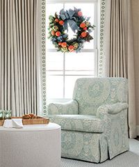 A light blue patterned armchair in front of a window with a Christmas wreath.