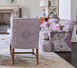 Two patterned armchairs in a living room, one with a detailed back, set on a patterned rug.