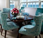 Dining room with turquoise patterned chairs and a table set for a meal. Ocean view in the background.