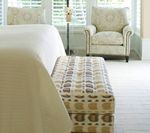 Bedroom with bed, patterned bench, armchair, and shuttered window.