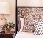 Bedroom with patterned headboard, lamp, pillows, and nightstand.