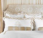 White bed with scalloped pillows trimmed in gold; monogrammed bolster pillows; ornate headboard.