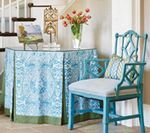 Teal chair beside a console table covered in blue patterned fabric, vase of red flowers.