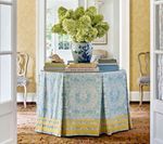 Round table with blue and yellow patterned skirt, vase of green flowers, flanked by chairs, doorway.