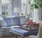 Blue patterned sofa and ottoman in a sunlit living room, with curtains and flowers.