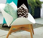 White scoop chair with wood legs, holds patterned pillows, outdoor setting.