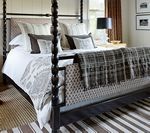 Four-poster bed with white linens and decorative pillows. Brown and gray accents. Striped rug.