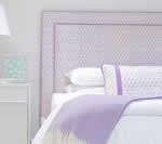 Lavender headboard with matching pillows and blanket on a white bed.