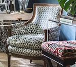 Armchair with patterned upholstery and wooden frame; a stool with a patterned top sits in front of it.