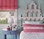 Bedroom with patterned wallpaper, pink roman shade, blue side table, and decorative headboard.