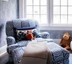 Blue patterned armchair with a stuffed fox and monkey, near a window.