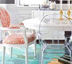 Dining room with a white round table, patterned chairs, and a clear chair on a teal and orange rug.