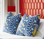Two blue patterned throw pillows on a bed against a red, padded wall.