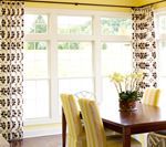 Dining room with large windows, patterned curtains, wooden table, and yellow upholstered chairs.