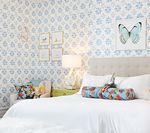 Bedroom with patterned blue wallpaper, white bed, artwork of butterflies.