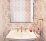 White sink with silver faucet and mirror, floral wallpaper. Towel on a holder, soap.
