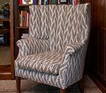 Wingback chair upholstered in a gray and white leaf pattern; sits in front of a bookshelf.