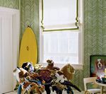 A child's room with green wallpaper, a window with a white shade, and a stuffed animal-covered chair.
