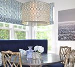Dining room with blue banquette seating, round table, gold chairs, and a patterned shade.