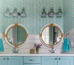 Bathroom with two round mirrors, turquoise cabinets, and light blue patterned wallpaper.
